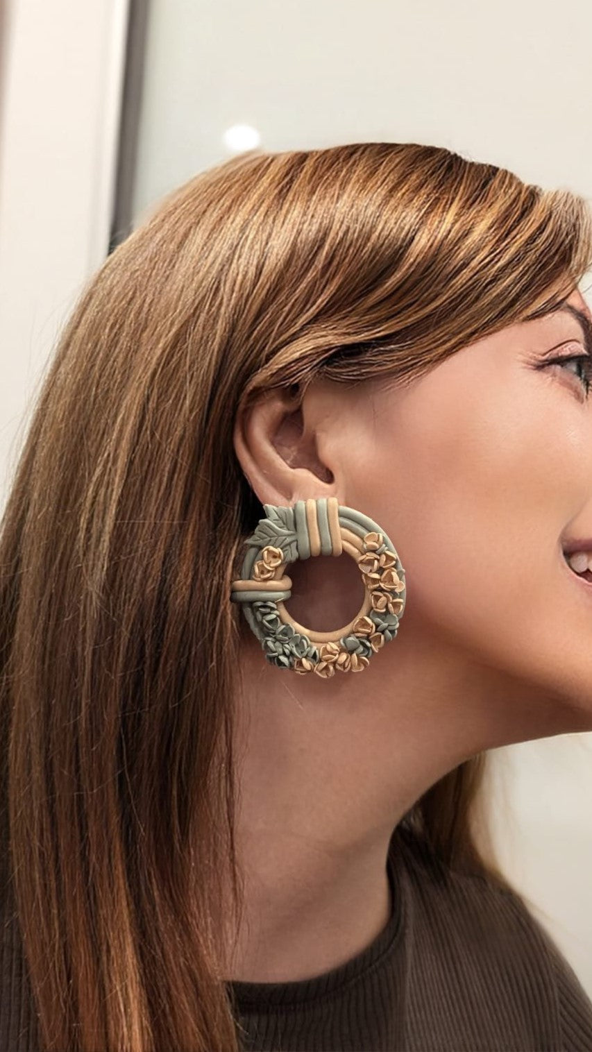 Handmade floral wreath polymer clay earrings in sage green and peach, styled on a model to showcase their elegant and lightweight design.