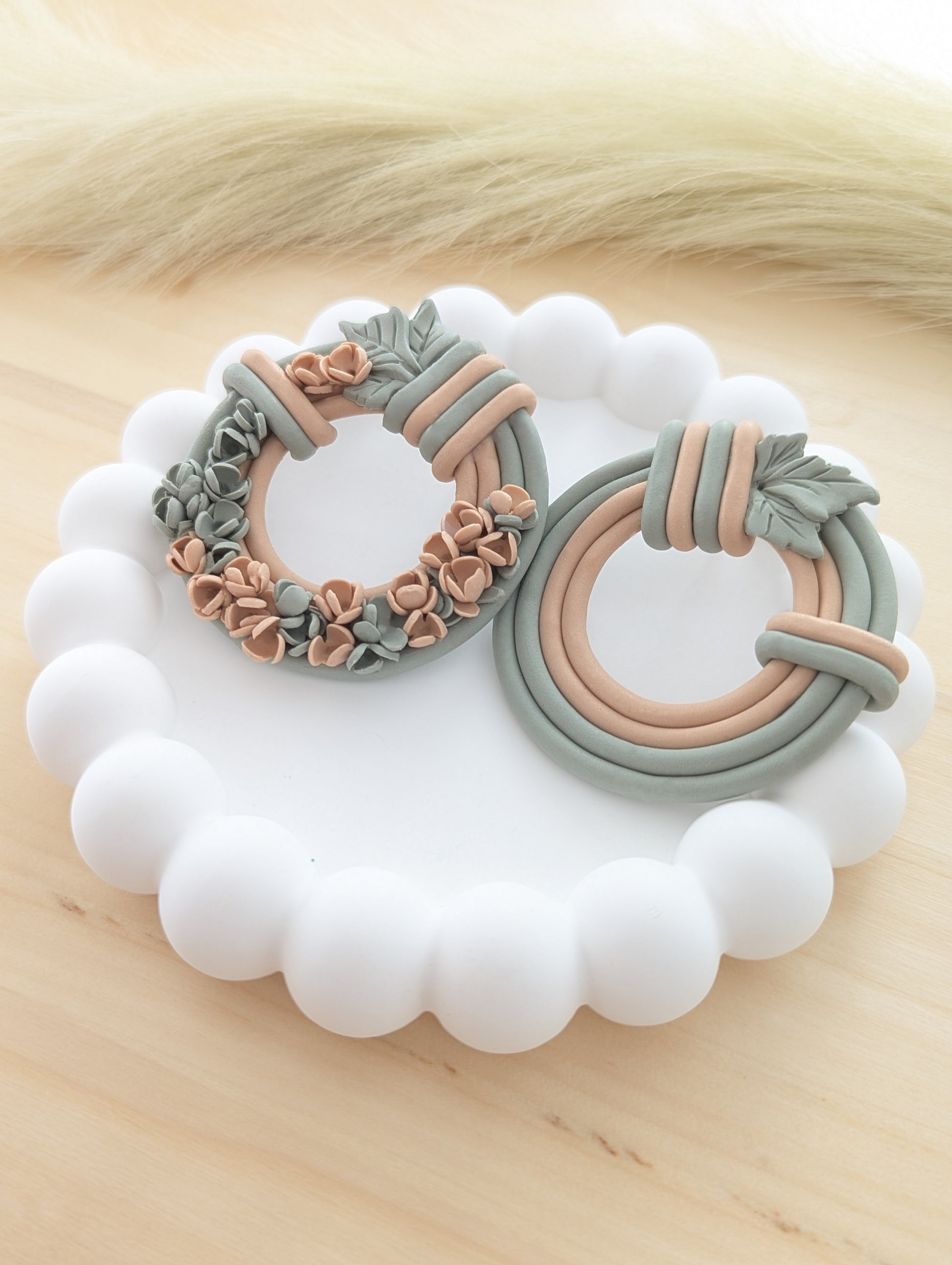 Close-up of floral wreath earrings, side by side, showcasing intricate flower and leaf details.