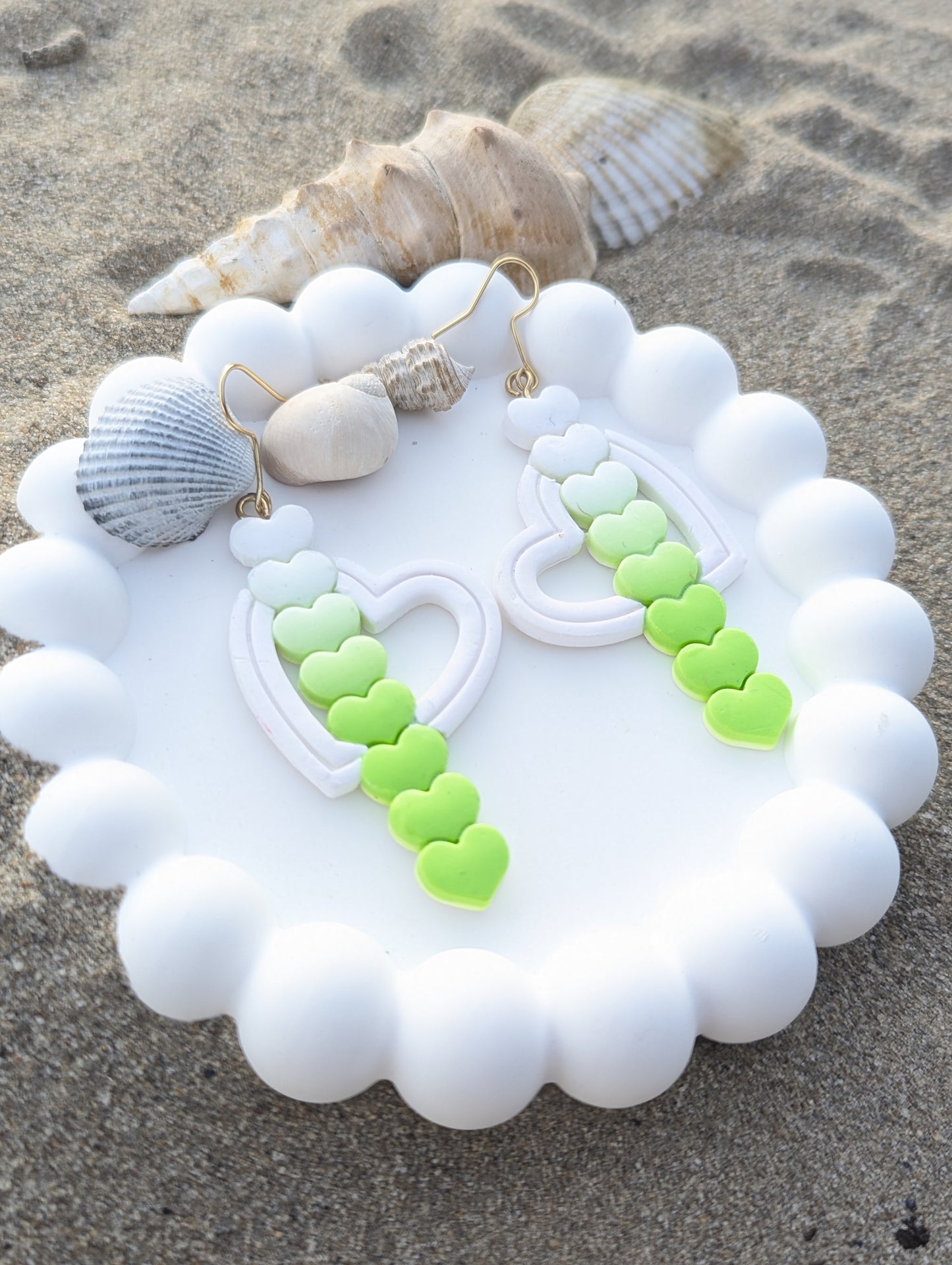 Handmade polymer clay earrings featuring a curved line of hearts in a white to lime green gradient crossing through an open heart, symbolizing a love arrow